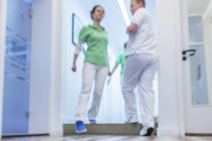 Personal einer Praxis, unscharf im Hintergrund, betritt oder verlässt eine Treppe, der Fokus liegt auf den Schachbrettfliesen.